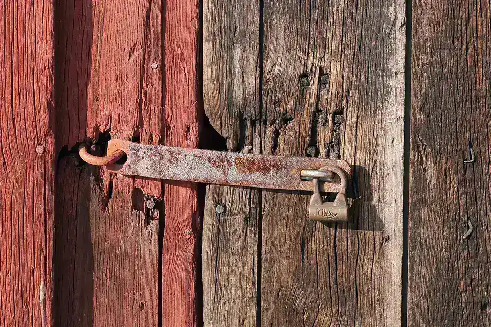 A rusty metal hasp and padlock fastening a weathered red wooden door