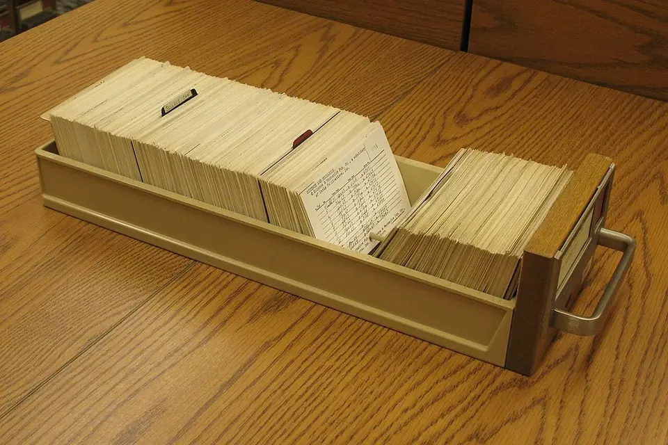 A metal drawer full of index cards from a card catalogue, resting on a wooden table